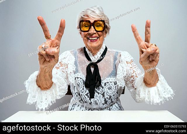 beautiful and elegant old influencer woman. Cool grandmother posing in studio wearing fashionable clothes. Happy senior lady celebrating and making party