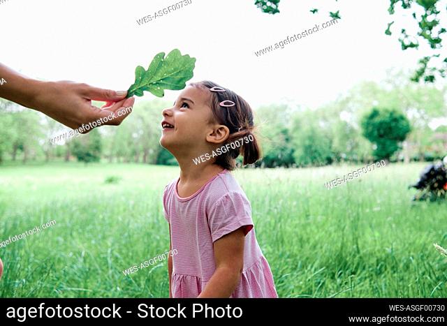 Hand of woman holding leaf by cute daughter at park