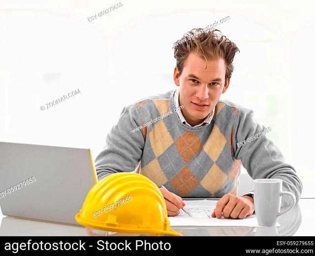 Young architect working on blueprint at desk, smiling