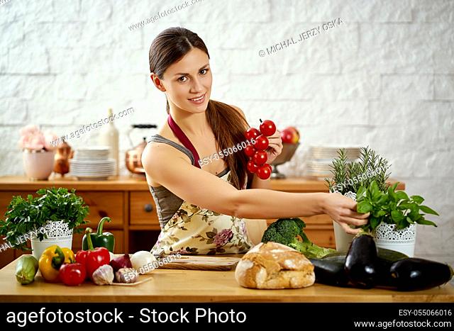 beautiful young woman, brunette holds tomatoes in the kitchen at a table full of organic vegetables