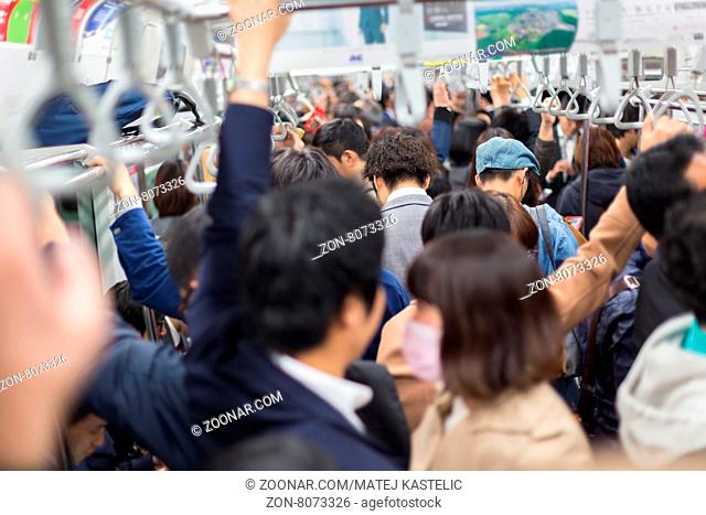 Passengers traveling by Tokyo metro. Business people commuting to work by public transport in rush hour. Shallow depth of field photo