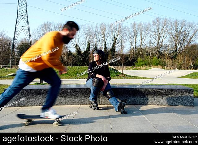 Mature man skating by friend sitting in park