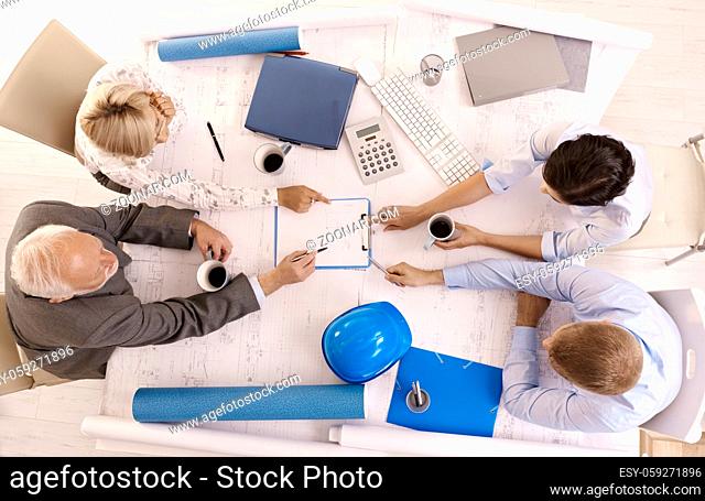 Businesspeople discussing work in office, sitting at meeting table, pointing at document, overhead view