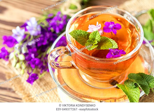 Glass cup of summer herbal tea with fresh mint and field larkspur. Wooden table. Shallow depth of field
