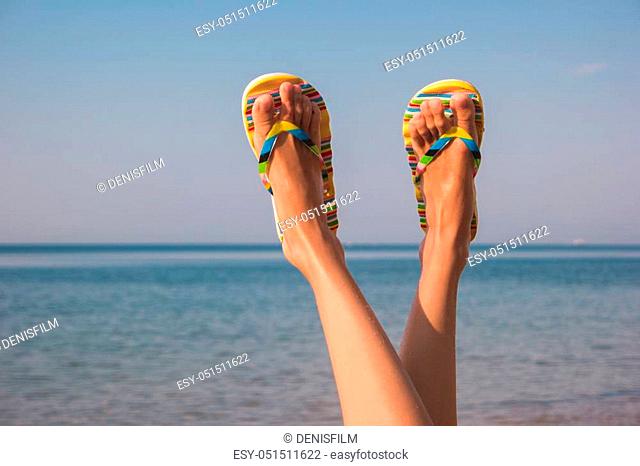 Female legs and sea. Feet in colorful flip flops. Away from bustle and noise. Get a tan
