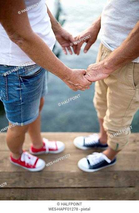 Senior couple holding hands on jetty, partial view