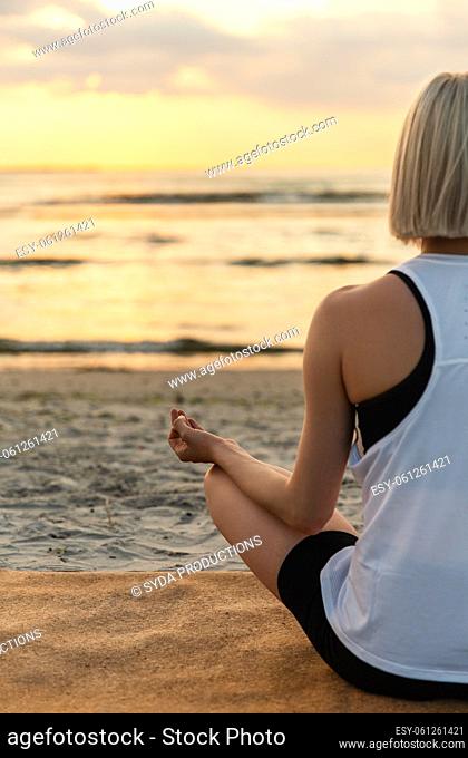 woman meditating in lotus pose on beach