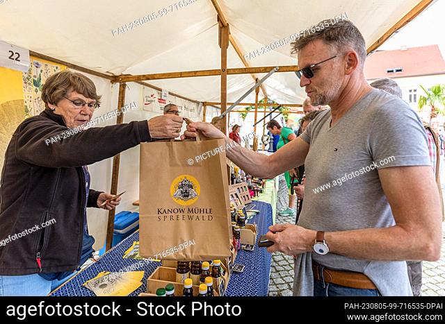 05 August 2023, Brandenburg, Golßen: A saleswoman hands a customer at a sales booth at the Spreewald Gherkin Day in Golßen a shopping bag with products...