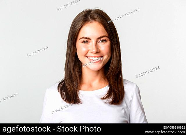 Close-up of attractive brunette girl smiling happy, standing white background