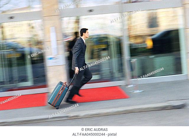 Businessman running down sidewalk, pulling suitcase behind him
