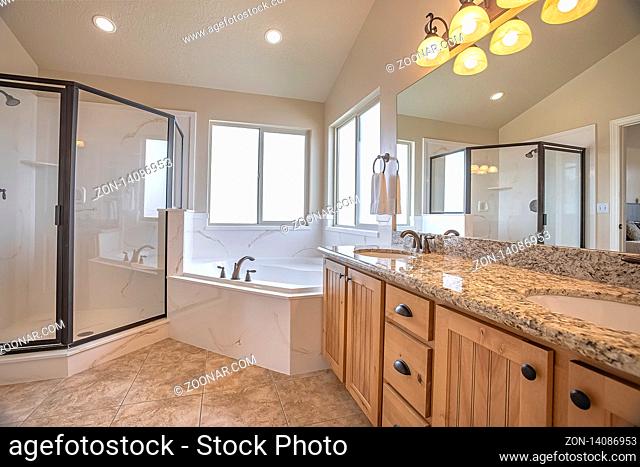 Shower stall bathtub and double vanity area inside the bathroom of a home. The room has white wall, tiled floor, and sliding windows