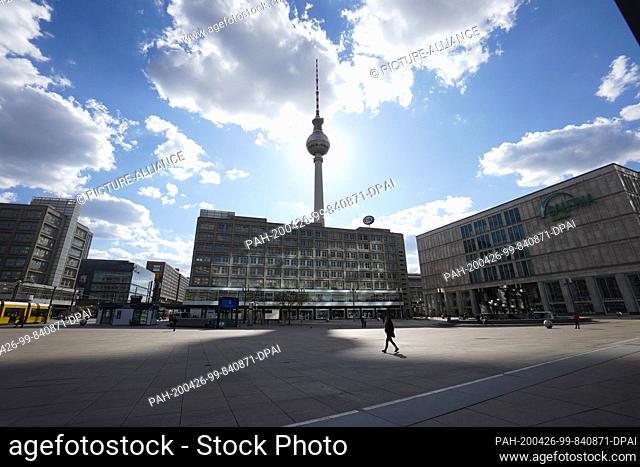 26 April 2020, Berlin: The television tower casts a huge shadow on Alexanderplatz, while a single person walks across the large square
