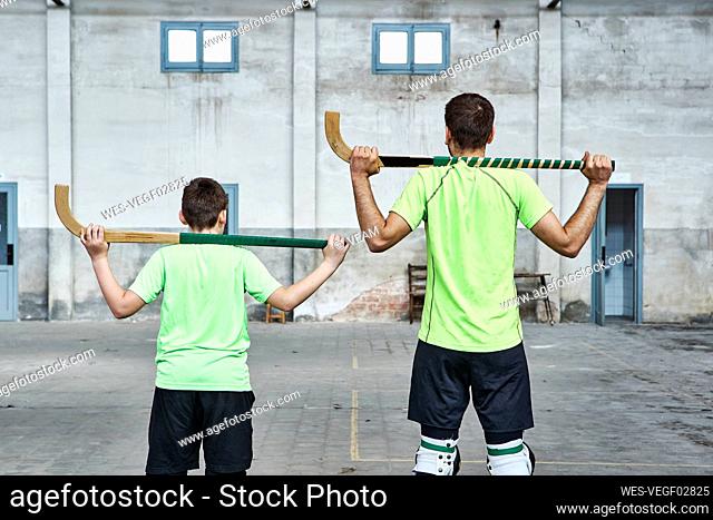 Father and son in uniform holding hockey sticks at sports court