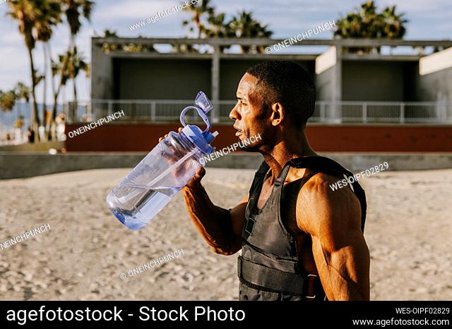 Thirsty sportsman standing with water bottle at beach