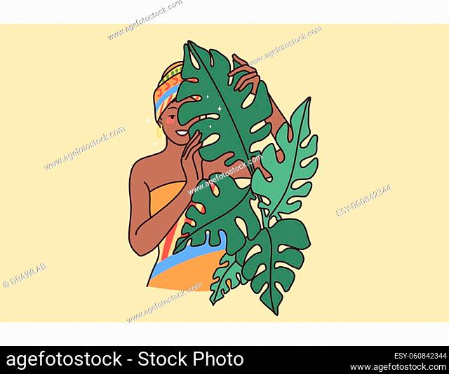 Young smiling African American woman in traditional clothes and turban. Happy black girl with scarf on head look behind leaves trees