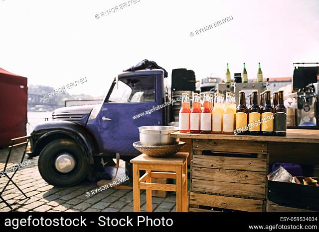 Lemonade, Cider And Other Drinks In Bottles Are Exhibited On A Wooden Counter Near Retro Truck With Food At Street Food Festival