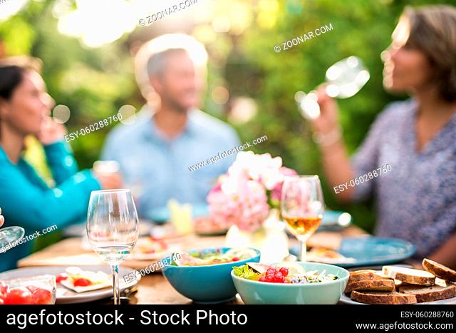 Focus on a colored salad in a bowl, Friends gather to share a meal around a table in the garden. Focus on the foreground