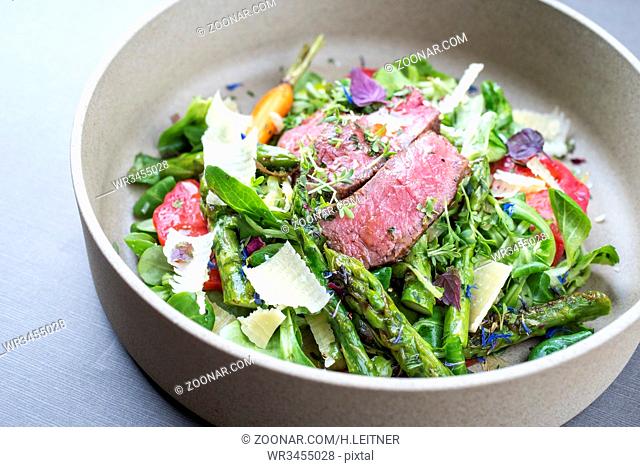 Modern spring salad with barbecue dry aged sliced fillet steak and green asparagus as top view on a plate