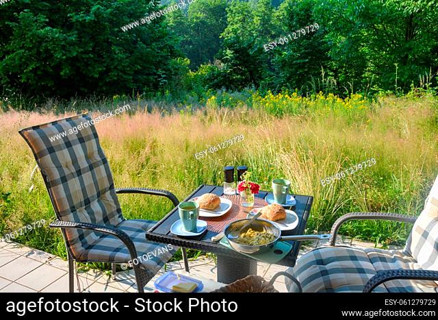Breakfast on the terrace in front of green nature on a beautiful summer day, with cup, fresh bread and table