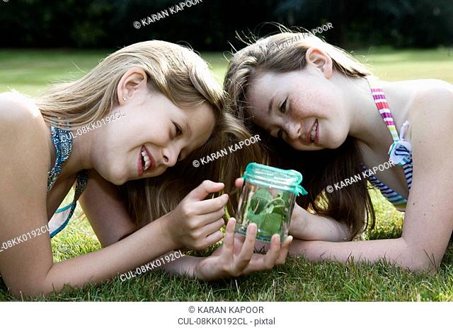 Two girls looking at jar with insects