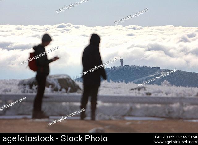 22 November 2023, Saxony-Anhalt, Schierke: Two hikers stand on the Brocken and look out over a sea of clouds. The landscape in the Harz National Park on the...