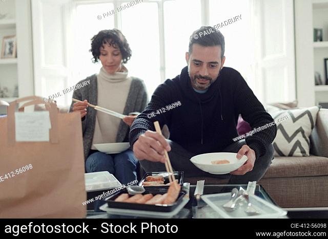 Couple enjoying takeout food with chopsticks in living room