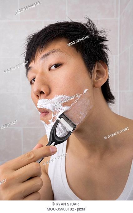 Portrait of mid adult Asian man shaving in bathroom
