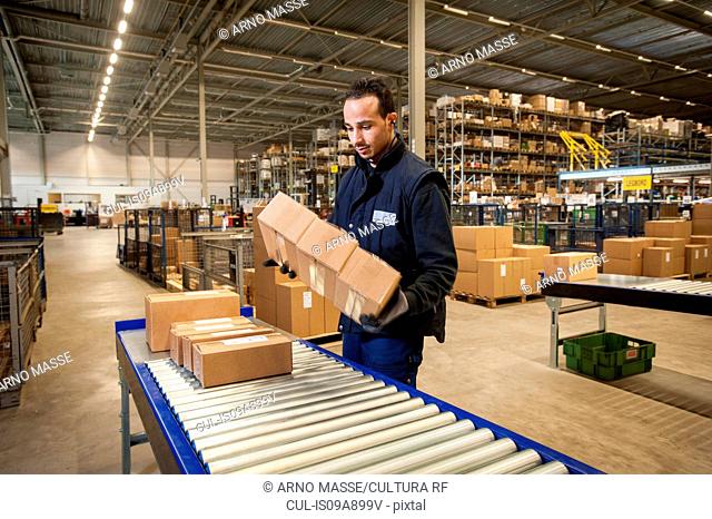 Male warehouse worker selecting cardboard boxes from conveyor belt