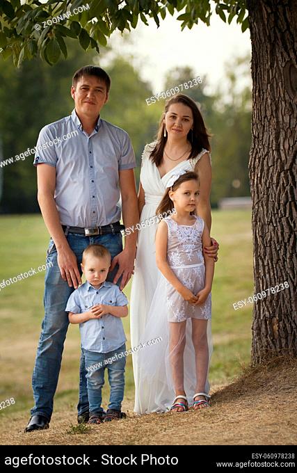 Cheerful family in a park at summer evening - father, mammy, daughter and little boy, portrait