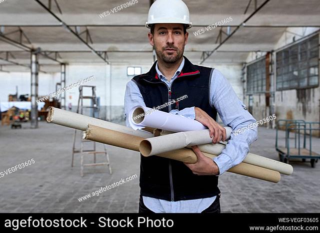 Confident male architect holding cardboards while standing in building