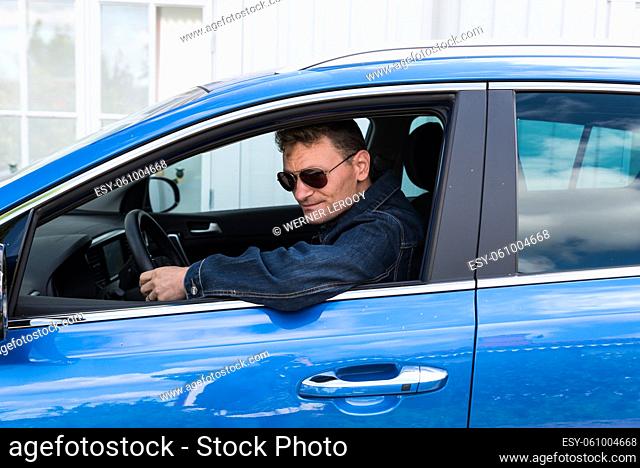 Oregrund, Uppland - Sweden - 30 07 2019- Fourty year old fashionable man with sunglasses posing in his blue Kia Sportage car