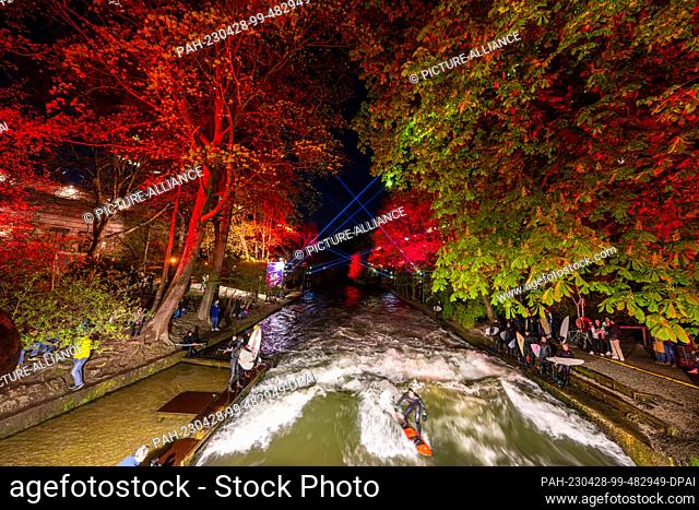 27 April 2023, Bavaria, Munich: A surfer rides his board on the artificial wave of the Eisbach in the English Garden, located in the heart of the Bavarian...
