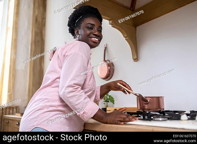 In the kitchen. Contented african woman in pink clothes cooking in the kitchen