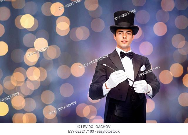 performance, circus, people and show concept - magician in top hat with magic wand over nigh lights background
