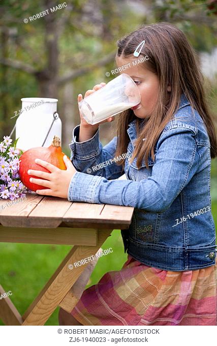 Girl drinking a glass of milk outdoor in the garden. Slovenian countryside