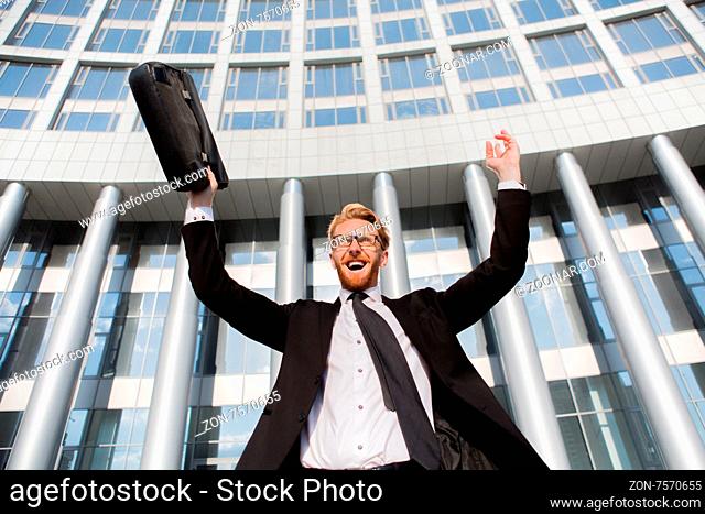 Successful businessman with arms up celebrating the victory. Smiling man in black business suit and brief case screaming from hapiness