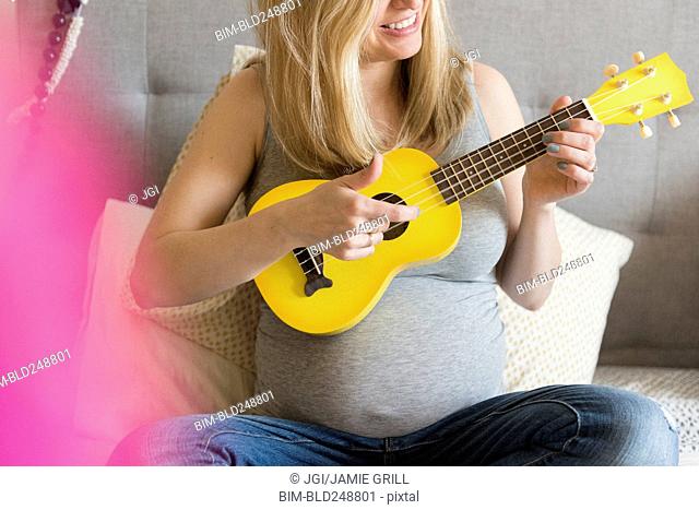 Caucasian and expectant mother playing small yellow guitar