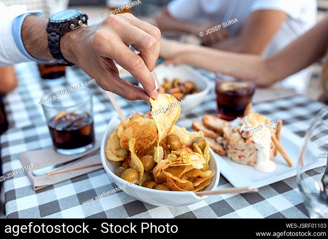 Cropped image of man having potato chip at cafe
