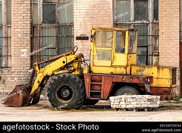 Old yellow broken bulldozer in the yard of abandoned factory