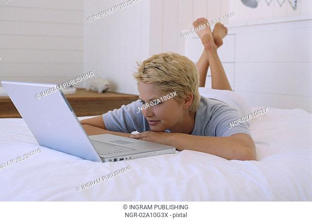 Young woman lying on a bed in front of a laptop