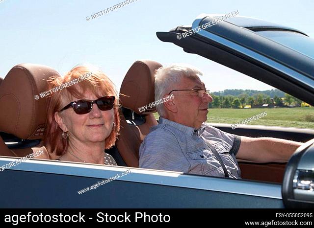 Happy senior couple with a luxury convertible car on a sunny day