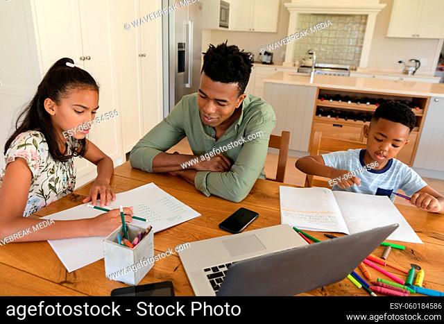 Happy african american father with daughter and son doing homework at home smiling