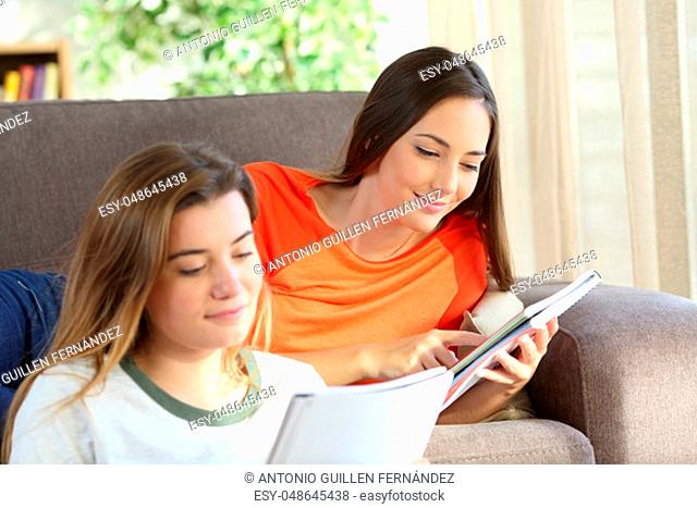 Two concentrated students learning reading notebooks on a couch in the living room at home