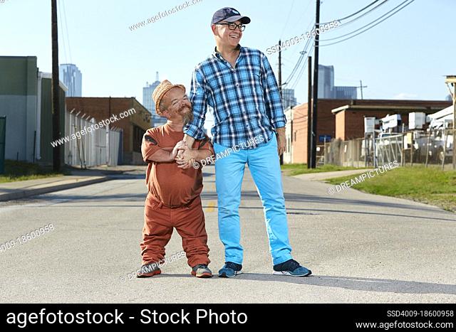 Portrait of male dwarf little person hugging his friend, standing in middle of street