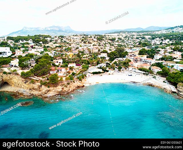 Distant view rocky coves, sandy beach, tiny bay of Benissa. Turquoise bright blue Sea waters hillside townscape at sunny day