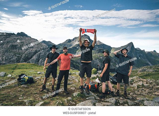 Norway, Lofoten, Moskenesoy, Group of young men cheering with Norwegian flag