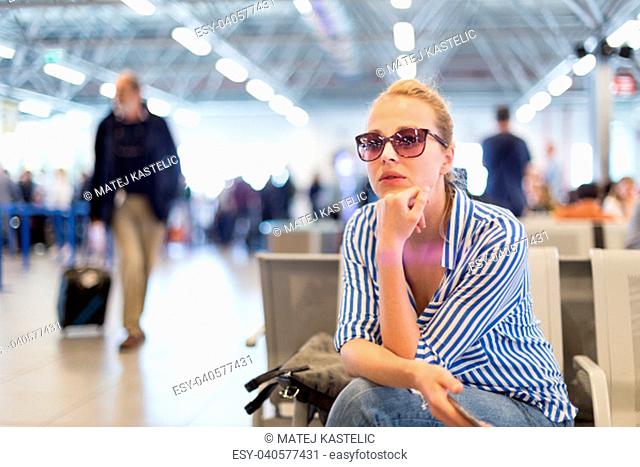 Casual blond young woman using her cell phone while waiting to board a plane at departure gates at international airport