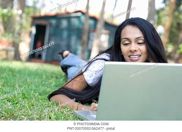 Close-up of a young woman lying down in a lawn and using a laptop