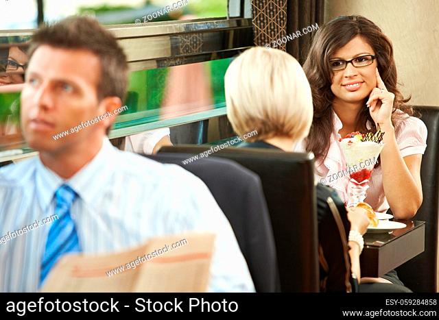 Young women sitting in cafe having sweets. Businessman reading newspaper in the forground. Selective focus on women