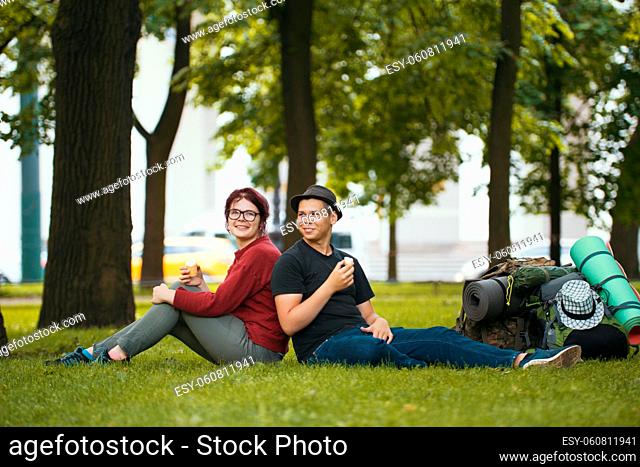 Young couple - man and woman - tourists with backpacks are eating the icecream in the park, telephoto shot